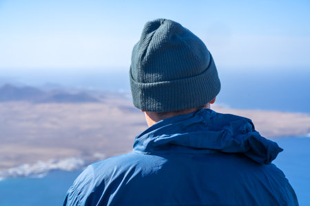 A man in a hat is looking on a beautiful landscape with ocean.