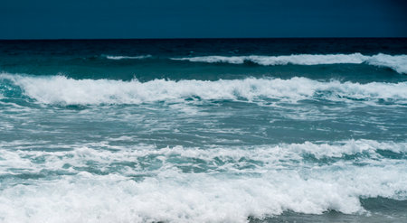 A sandy beach on the coastline of the ocean with clear water with small waves.