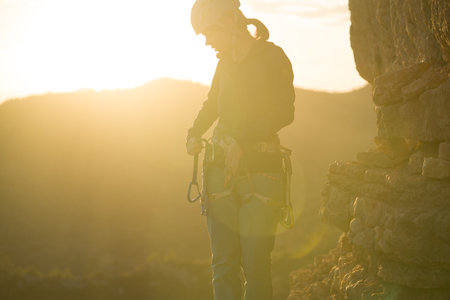 Young girl is preparing for training on the rocks sunset, in the mountains and puts a helmetの写真素材