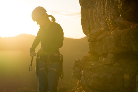 Young girl is preparing for training on the rocks sunset, in the mountains and puts a helmet