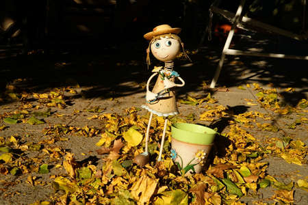 Doll with scissors and a pot in the garden between leafs in autumn.の写真素材