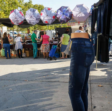 Street market in Madrid, Spain. Mannequin with trousers, a stand with umbrellas and people buying.のeditorial素材