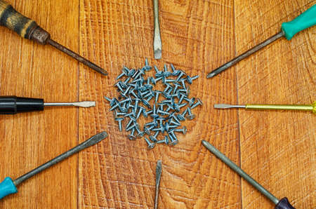 Many screwdrivers and screws closeup on background of wooden planks.