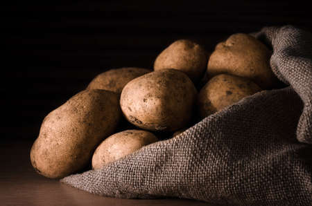 Fresh potatoes in the sack close-up on a dark wooden backgroundの写真素材