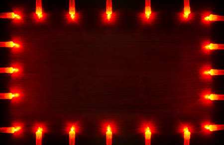 Glowing orange garland in the form of candles against a dark red wooden backgroundの写真素材