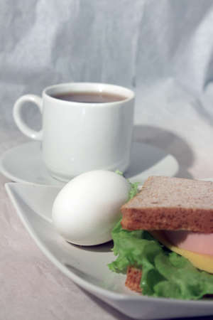 An egg and a sandwiche on a plate and a cup of tea  against light backgroundの写真素材
