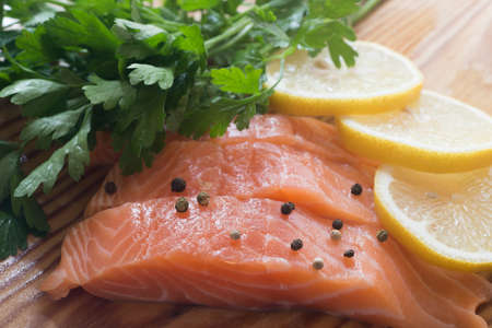raw salmon with parsley, pepper and lemon on wooden tableの写真素材