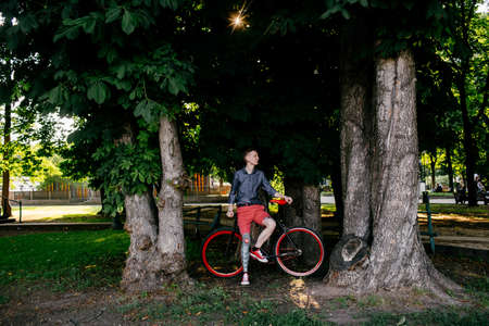 Hipster with red bycicle and tattoo on leg in parkの写真素材