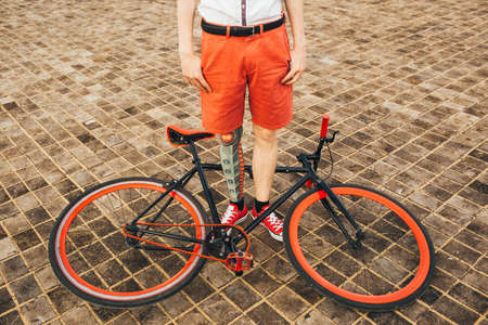 Red bycicle is on the square floor and boy with tattoo on his legの写真素材