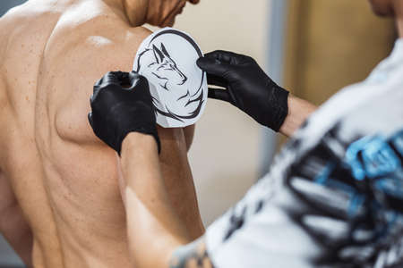 master tattooist makes a tattoo on the skin of the client in a workshop with special equipmentの写真素材