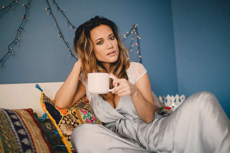 Young beautiful woman drink coffee at home lying on bed.の写真素材