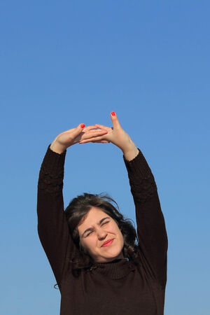 Young woman stretching arms outdoors on blue skyの写真素材
