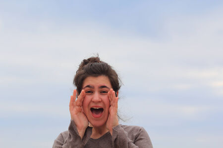 Young woman shouting, with hands on mouthの写真素材