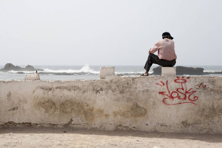 Single man sitting and looking at the sea with a capの写真素材
