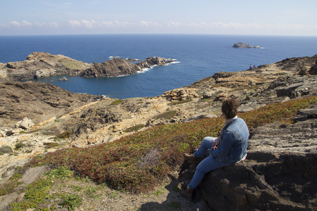 Young woman looking to the sea, sitting in a rockの写真素材