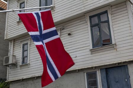 Norwegian flag in the street, with a traditional wooden white house in the background, Norwayの写真素材