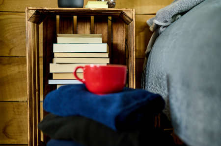 Books on the shelf with pile of clothes and red cupの写真素材