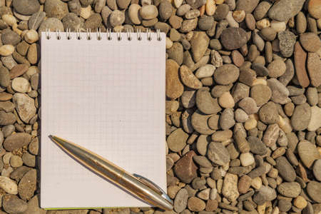 Open white note book on rings with metal ball pen on the pebble beachの写真素材