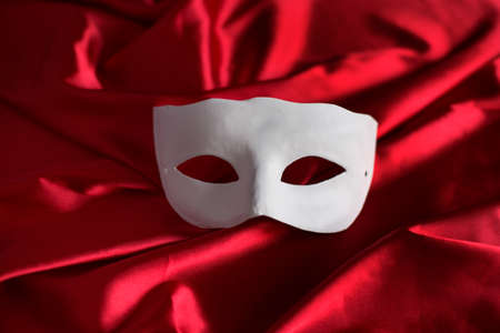 White mask lying on red satinの写真素材