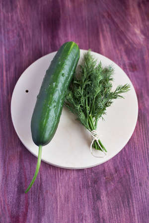 One fresh cucumber and bunch dill lying on a light plateの写真素材