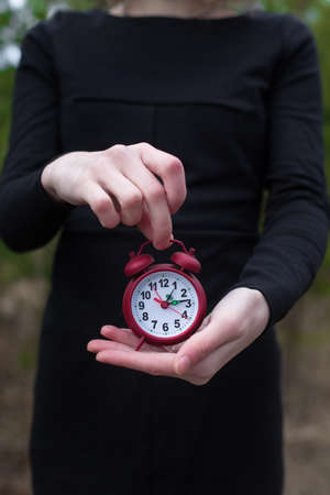 Women in black dress holding red alarm clock by one handの写真素材