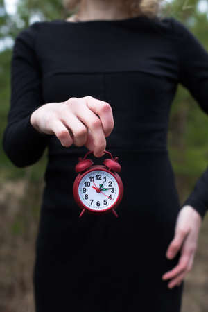 Women in black dress holding red alarm clock by one hand onlyの写真素材
