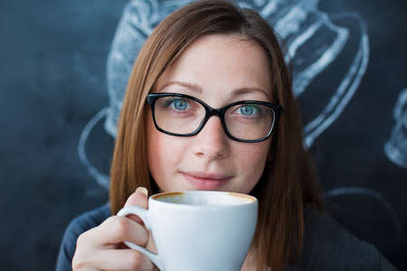 Girl holding a cup of coffee and looking at cameraの写真素材