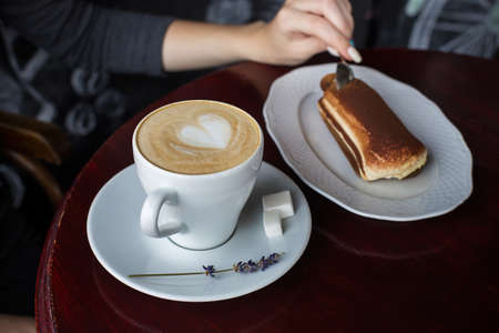 A cup of coffee with foam and a tiramisu cake on the tableの写真素材