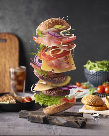Delicious burger with flying ingredients on kitchen table over dark concreate backgroundの写真素材