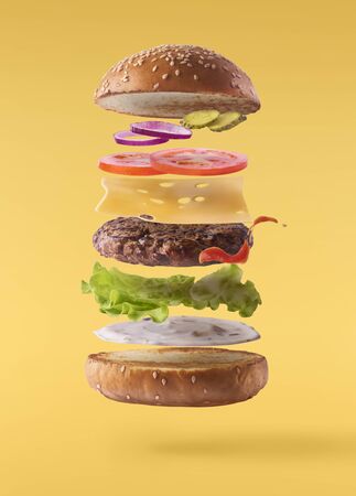 Delicious burger with flying ingredients isolated on yellow backgroundの写真素材
