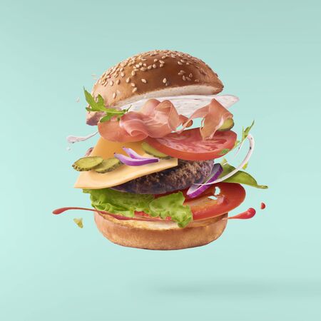 Delicious burger with flying ingredients isolated on turquoise backgroundの写真素材