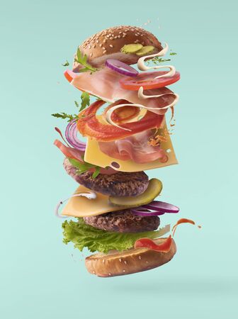 Delicious burger with flying ingredients isolated on turquoise backgroundの写真素材