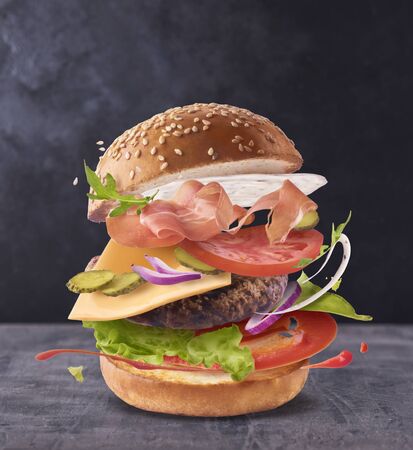 Delicious burger with flying ingredients on dark concreate backgroundの写真素材
