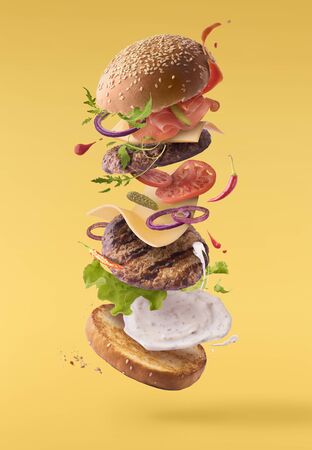 Delicious burger with flying ingredients isolated on yellow backgroundの写真素材