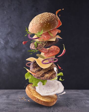 Delicious burger with flying ingredients on dark concreate backgroundの写真素材