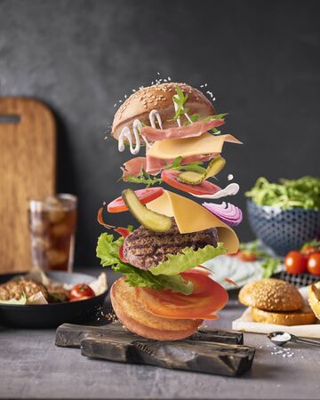 Delicious burger with flying ingredients on kitchen table over dark concreate backgroundの写真素材