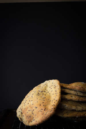 Wholemeal Pita Bread with Seeds Stacked on Table with Dark Background and Copy Space