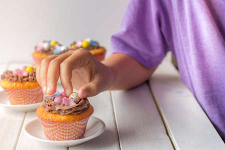 Easter Cupcakes Decorated with Easter Eggs and Wafer Flowers with Boys Hand Taking Easter Egg Table Horizontal Selective Focusの写真素材