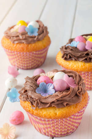 Easter Cupcakes on White Wooden Table Decorated with Easter Eggs and Wafer Flowers Vertical...