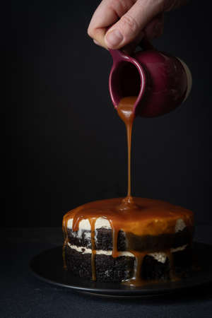 Pouring Caramel Sauce over a Salted Caramel Chocolate Cake - Vertical. 