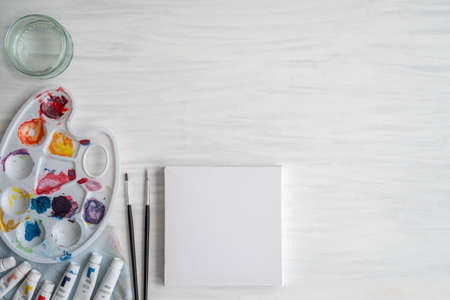 Flat Lay of Artist Workspace with Acrylic Paints, Brushes and Blank Canvas Ready to Paint with Copy...