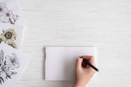 Hand of Artist in Workspace with Sketches, Pen and Blank Sketch Pad Ready to Draw with Copy Spaceの写真素材