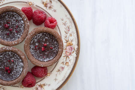 Plate with Delicious Chocolate Tarts from Above on White Background with Copy Space