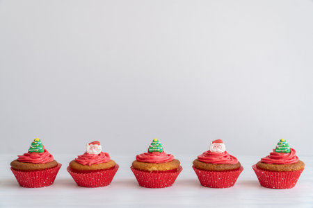 Red Christmas Cupcakes with Santa and Tree Toppers in a Line on Table with White Background and Copy Spaceの写真素材