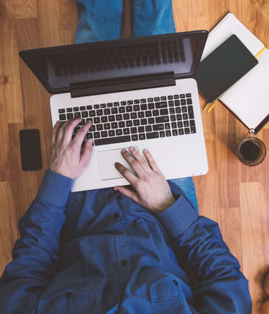 Man working on a wooden floor with his laptop, phone, tablet and agenda.の写真素材