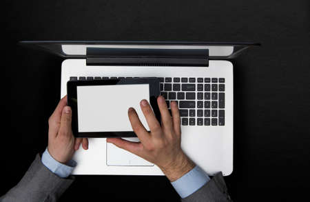 Business man typing on a pc tablet near a laptop, dark background.の写真素材