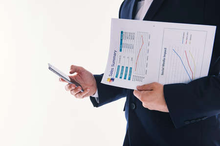 Man with a business report typing at his smartphone.の写真素材