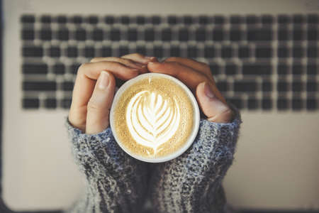 Coffee break concept - girl holding a cup o coffee with a laptop in background - hipster toneの写真素材