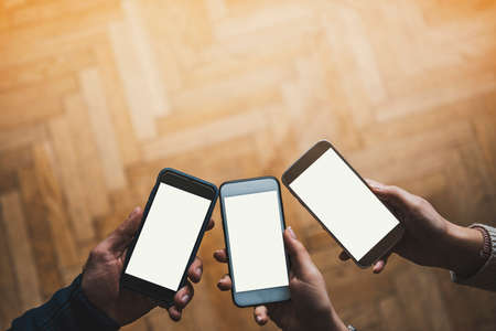 Three hands holding smart phonesの写真素材