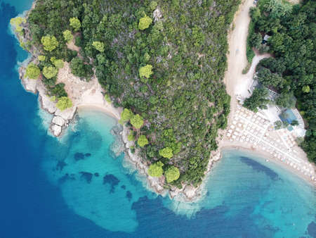 Aerial view of bright turqoise water and beach with pine forest.
